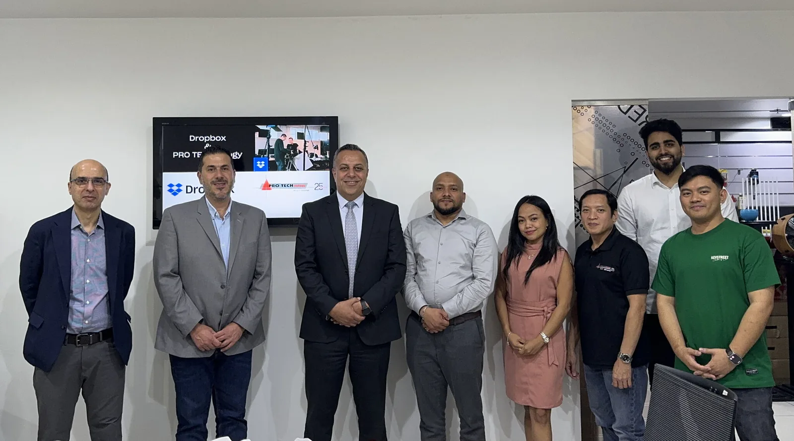 Dropbox and PRO TECHnology teams standing together at a joint working session in PRO TECHnology's Dubai office, with the Dropbox and PRO TECHnology logos on the screen behind them
