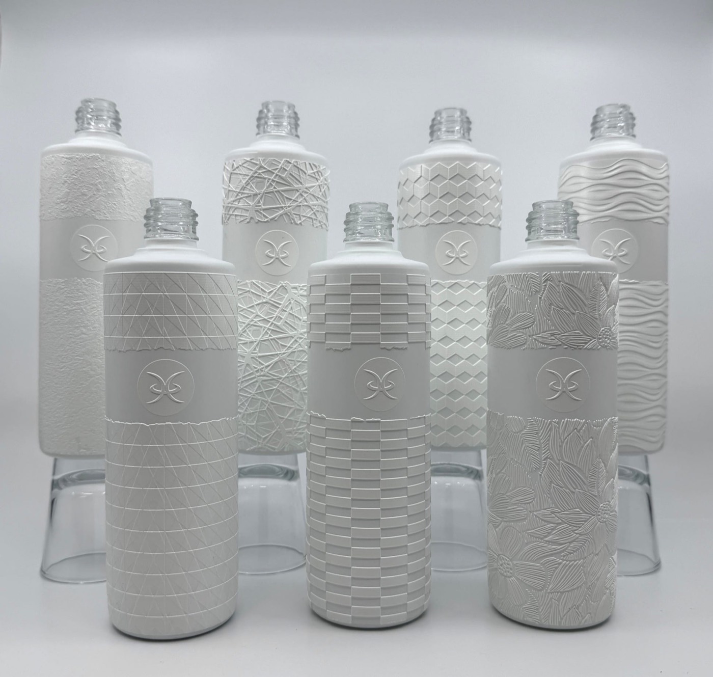 A range of bottles printed with different raised textured finishes, each pattern built up from cured ink on the container surface