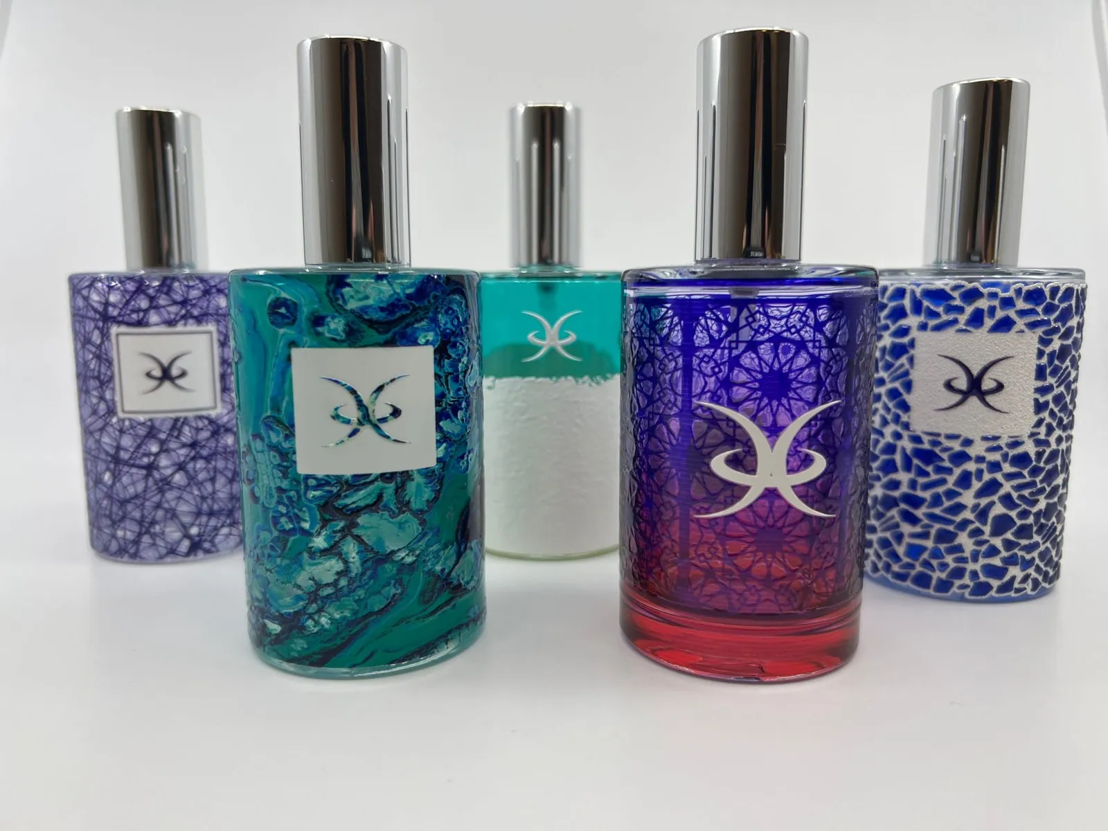 Five glass perfume bottles with silver caps, each printed with a different full-wrap pattern: purple lines, turquoise marble, white texture, purple and red gradient, and a blue mosaic