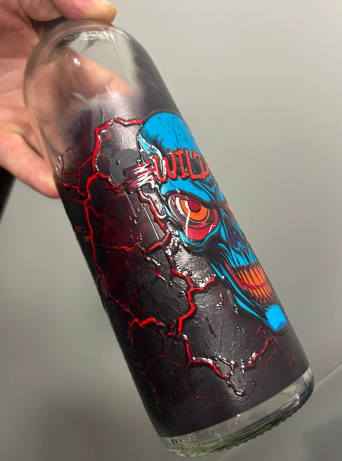 Clear glass bottle printed on an LSINC cylindrical UV printer, with raised tactile relief along the red crack detail and the unprinted glass visible at the neck and base