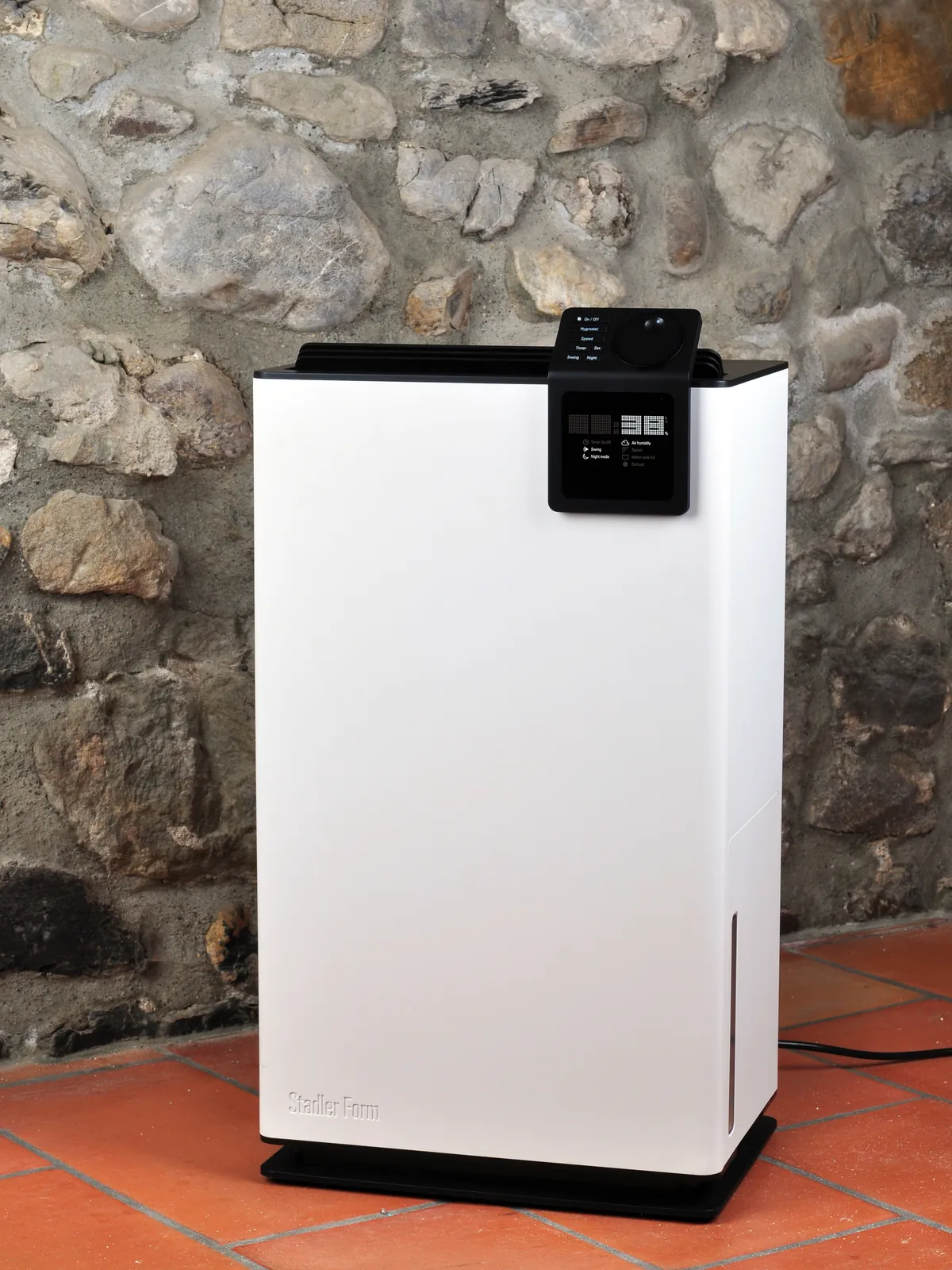 Stadler Form Albert dehumidifier standing on a terracotta floor against a rustic stone wall
