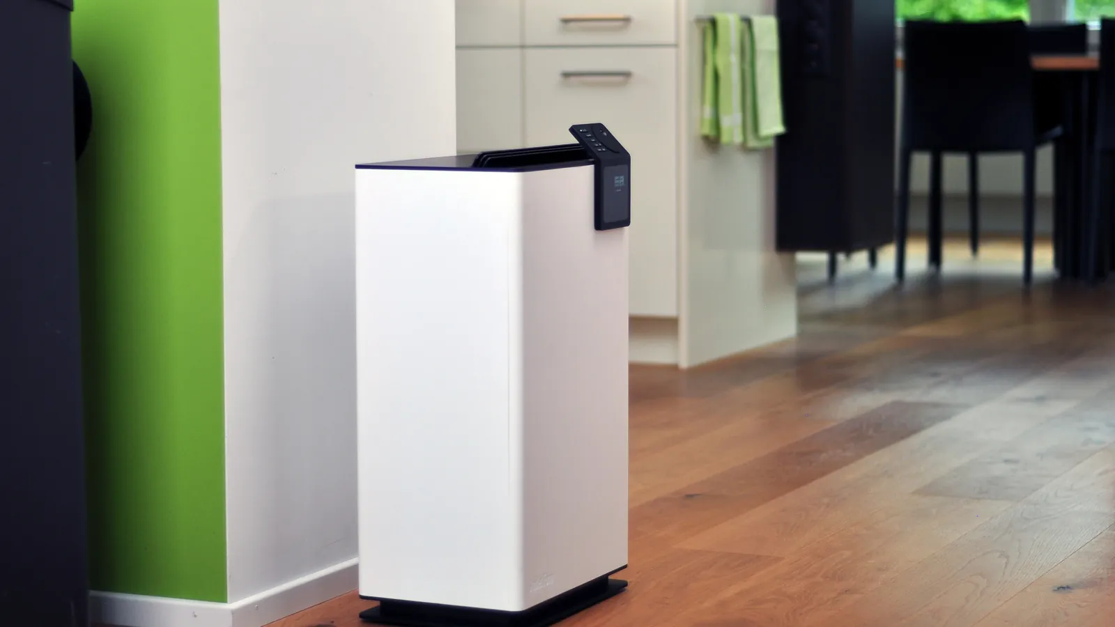 A white Stadler Form Albert dehumidifier standing on a wooden floor in a modern kitchen with a green accent wall
