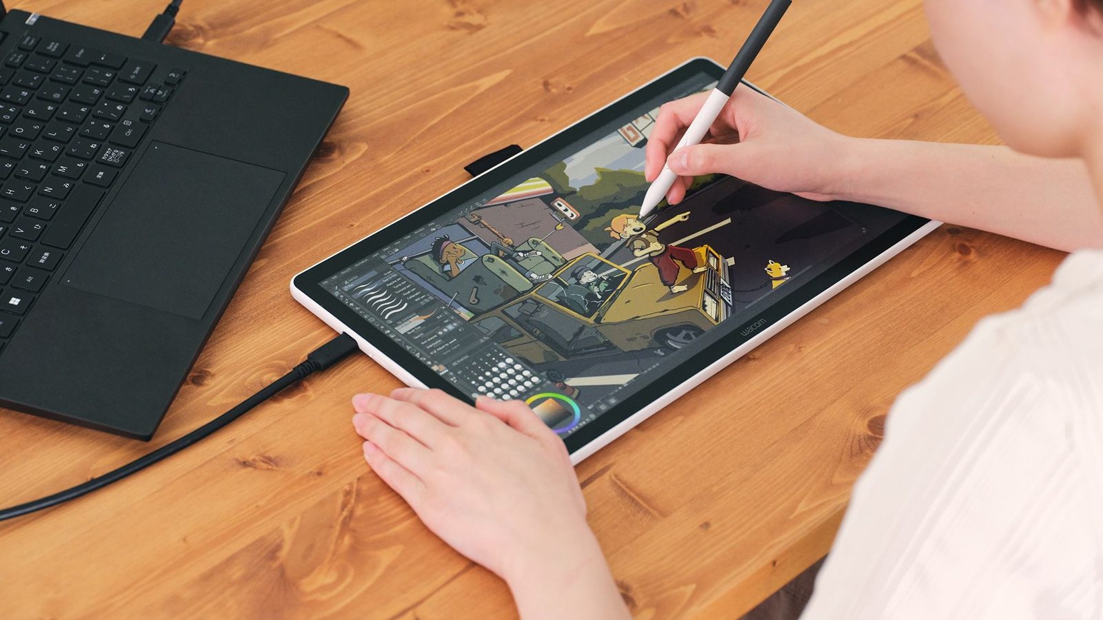 An artist drawing on a Wacom One 14 pen display beside a laptop, illustrating a guide to choosing a Wacom drawing tablet, pen display or signature pad in the UAE