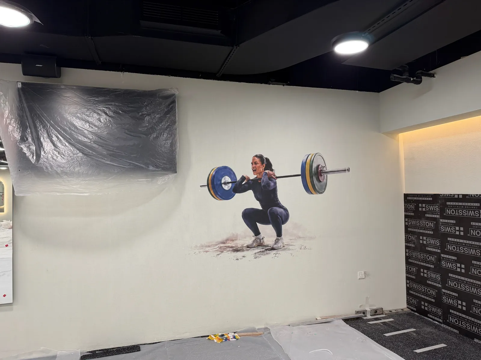 Weightlifter printed on a gym wall, with a wall screen and the floor wrapped in protective plastic