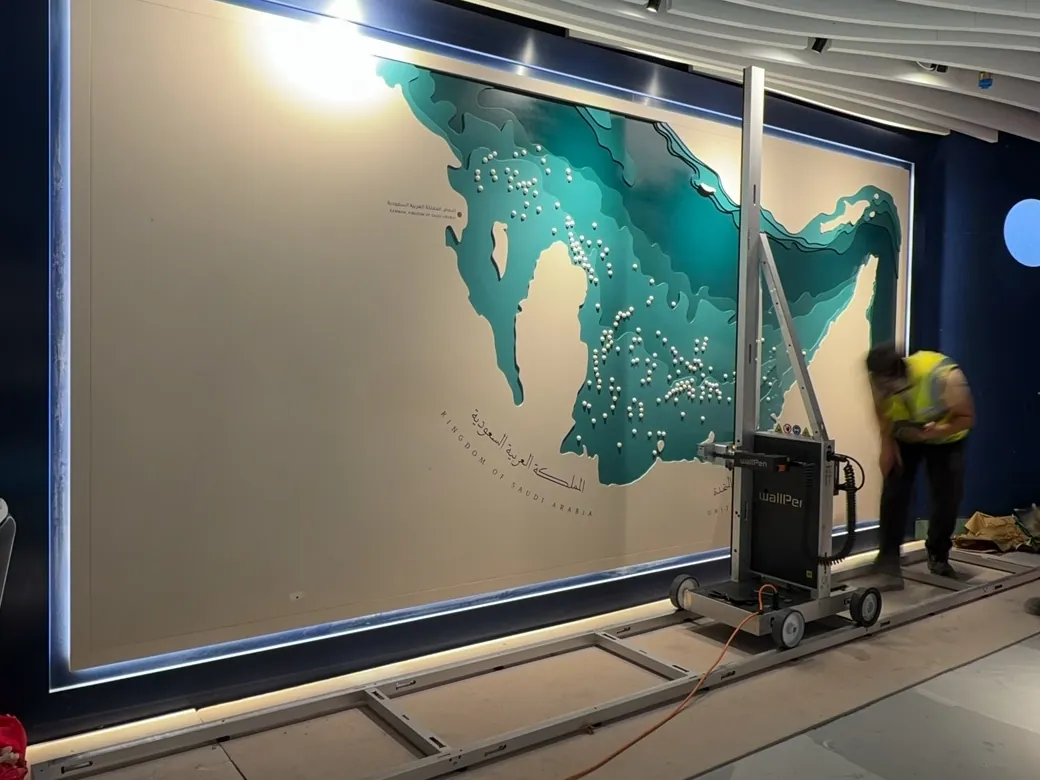 A wallPen printer on floor rails in front of an installed map panel, part of the lettering already printed, an operator beside the machine