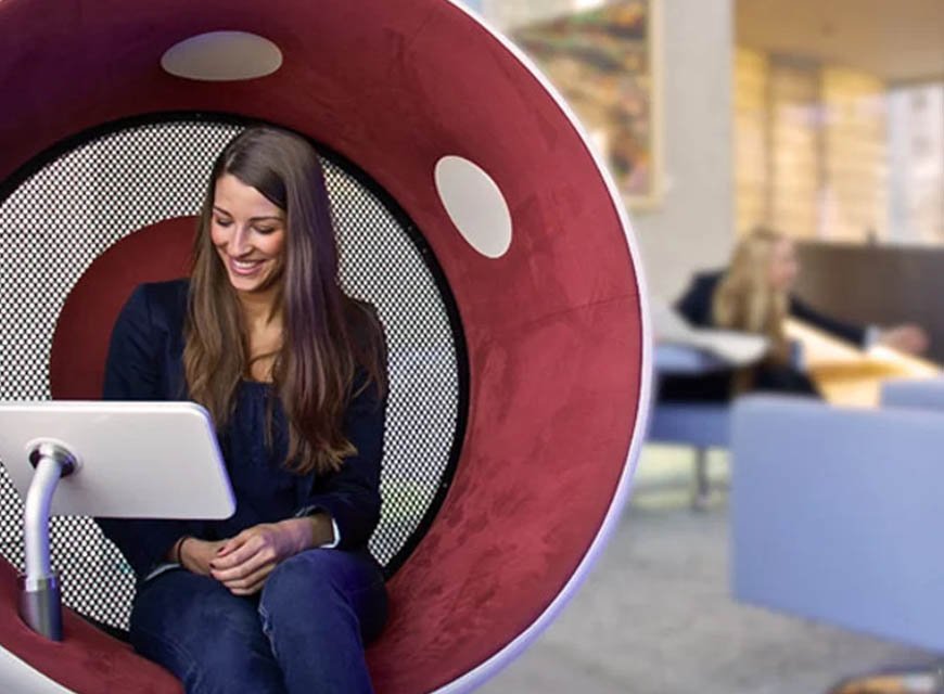 Woman using a tablet inside a red spherical sonic chair with built-in speakers in a lobby