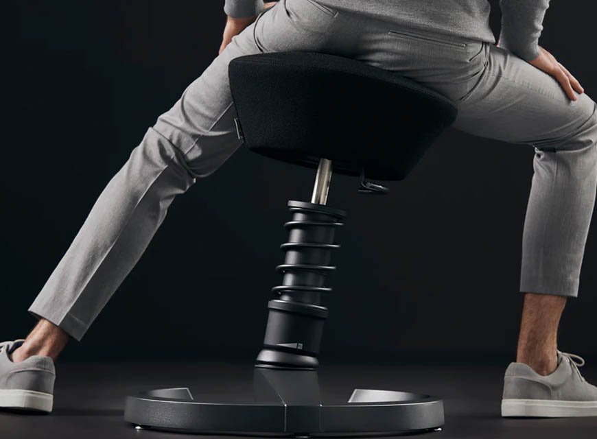 Office worker perched on a black Aeris Swopper stool with its spring strut flexing
