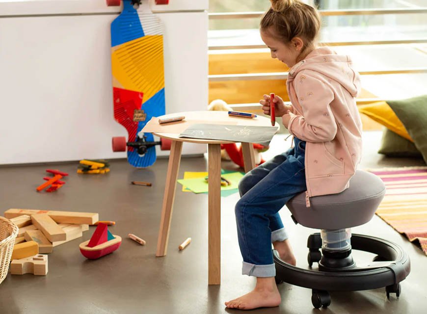 Child drawing at a table while sitting on a grey Aeris Swoppster swivel chair