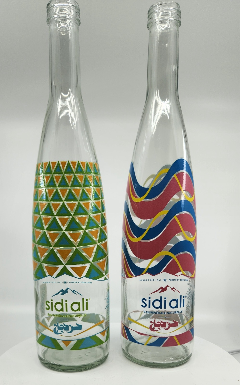 Two glass water bottles printed direct onto clear glass with geometric and wave artwork, with no label applied