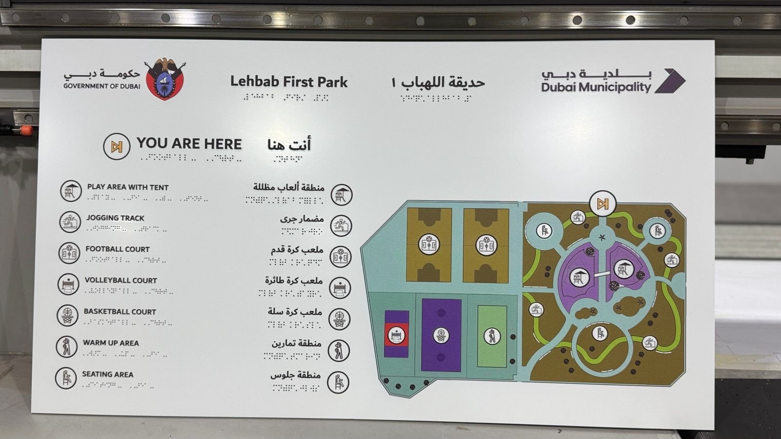 Dubai Municipality park wayfinding panel on the flatbed bed, bilingual amenity list and colour site map with raised tactile braille under every line