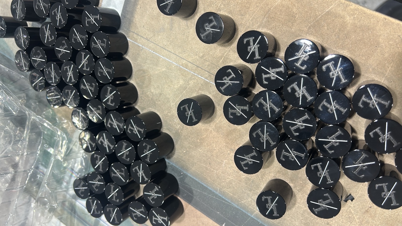 A production batch of small black plastic caps and discs, each printed with the same silver crossed tools monogram