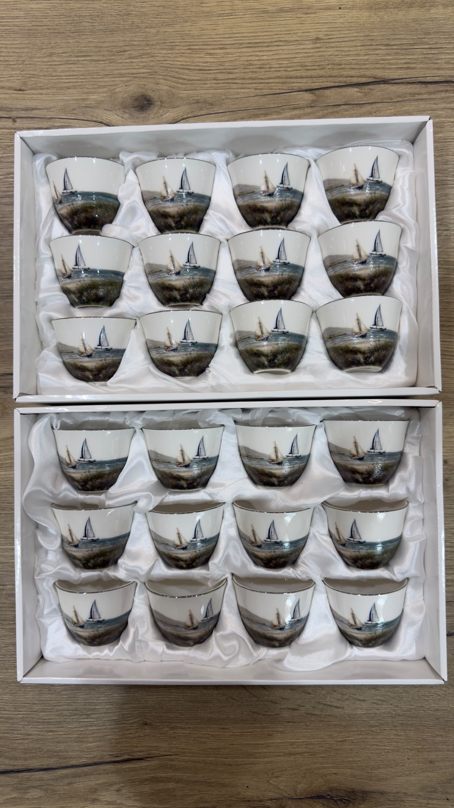 Two presentation boxes of printed porcelain qahwa cups, each cup carrying a photographic seascape with sailing boats
