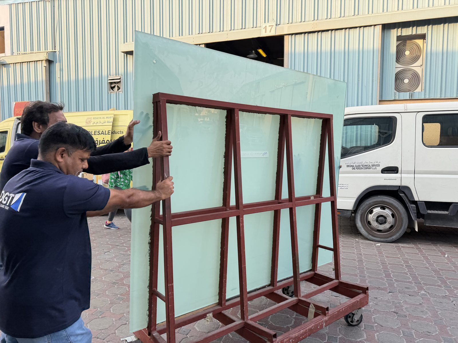 A large glass panel flood printed in a colour-matched light blue, moved on an A-frame trolley outside Sun Studio in Al Quoz, Dubai